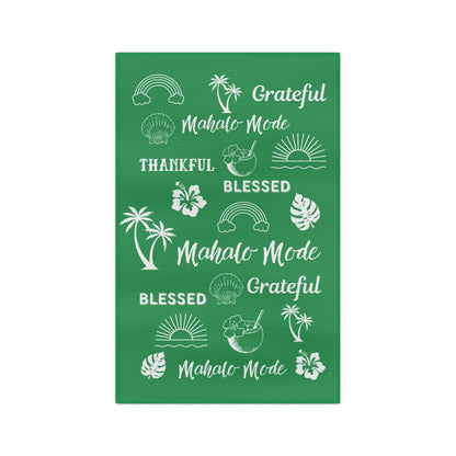 A green kitchen towel with white tropical-themed illustrations and phrases including 'Grateful Mahalo Mode,' 'THANKFUL,' 'BLESSED,' and 'Mahalo Mode,' shown on a plain white background.