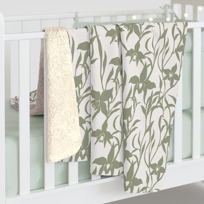 Sage green orchid-and-leaf print sherpa fleece blanket with a warm white background and rounded corners draped on a white crib.