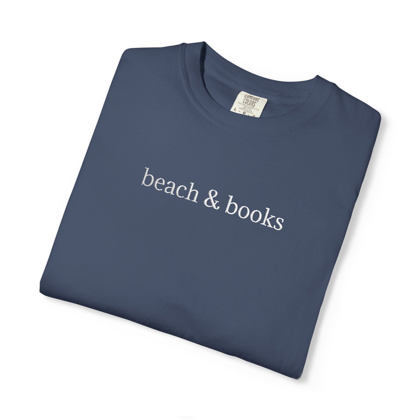 A folded blue comfort colors tee with 'beach & books' embroidered in white