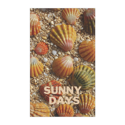 A tea towel featuring a close-up photograph of scallop sunrise shells on sandy ground, with the words “SUNNY DAYS” printed across the lower center. The design is centered on a white background.