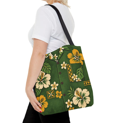 A woman wearing a white t-shirt and black pants carries a green tote bag with a yellow and white hibiscus floral pattern and a black shoulder strap, shown from a side-back angle against a white background.
