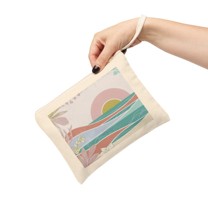 A hand with black nail polish holds a cream canvas pouch featuring a colorful abstract landscape print with a pink sun, teal waves, and green foliage, set against a plain white background.