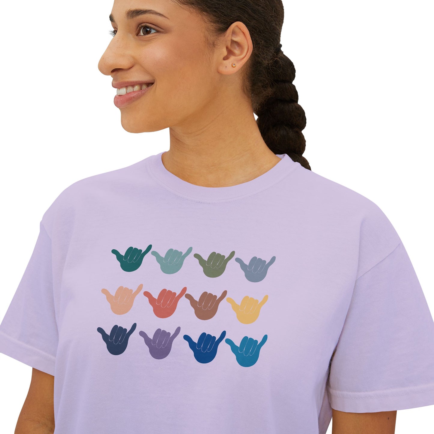 A woman wearing a light lavender crewneck t-shirt with a graphic of twelve shaka signs in various colors arranged in a grid.