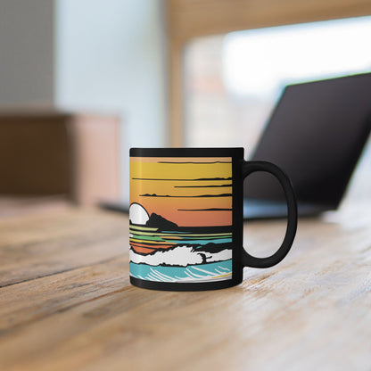 Summer Sunrise black coffee mug with Kaʻōhao Hawaiʻi inspired artwork by Global Village Kailua sitting on wood table with laptop blurred in background.