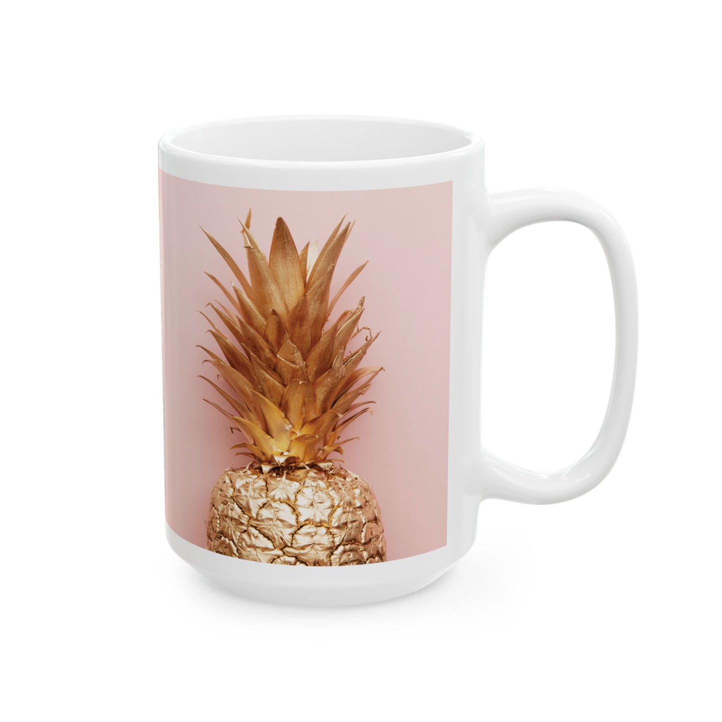 A white ceramic mug featuring a printed graphic of a golden pineapple on a dusty pink background, shown against a clean white studio backdrop.