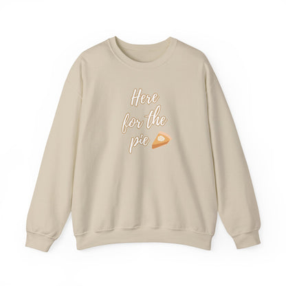 A light beige crewneck sweatshirt with a graphic on the chest reading 'Here for the pie' in white script next to a small slice of pumpkin pie illustration.
