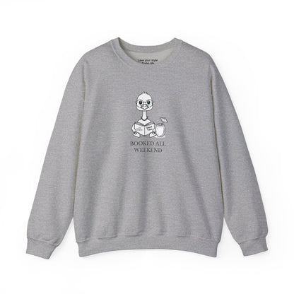 Gray sweatshirt with graphic print of a cartoon nene goose sitting reading a book with a cocktail next to it with text 'BOOKED ALL WEEKEND'