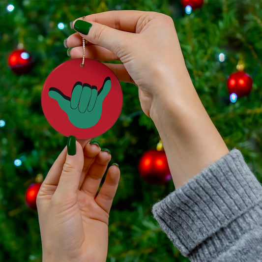 Red ceramic Christmas ornament featuring a green shaka hand design with black outline.