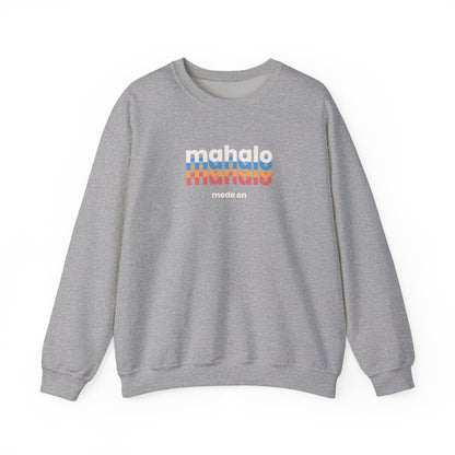 A heather gray crewneck sweatshirt featuring a retro-style chest graphic with the word 'mahalo' repeated in white, blue, and orange, with 'made an' printed below in small white text.