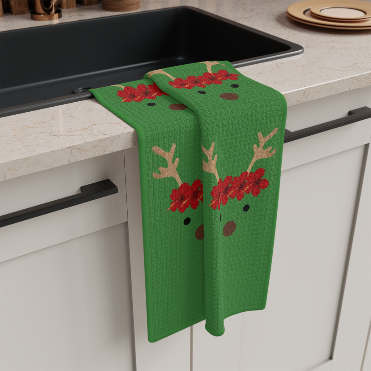Green Reindeer and Rudolph holiday kitchen towel with red nose design hanging off a kitchen sink