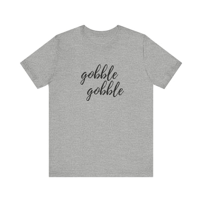 A grey short-sleeve crewneck t-shirt featuring the phrase 'gobble gobble' printed in black cursive script across the chest, displayed against a solid white background.
