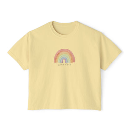 A pale yellow short-sleeve crop top t-shirt featuring a pastel rainbow graphic and the text 'ALOHA VIBES' printed on the chest, displayed against a solid white background.
