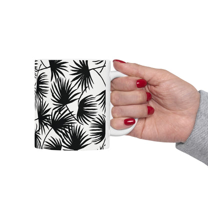 A hand holding a Palm Fan Black coffee mug with black and white tropical palm print by Global Village Kailua