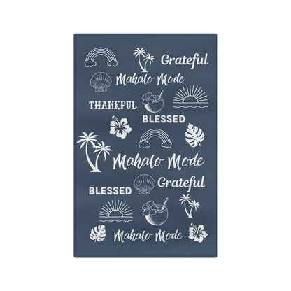 A denim blue kitchen towel with white tropical-themed illustrations and phrases including 'Grateful Mahalo Mode,' 'THANKFUL,' 'BLESSED,' and repeated 'Mahalo Mode' text, shown on a plain white background.