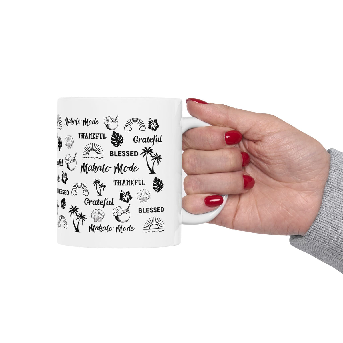 A white ceramic mug with black tropical-themed text and illustrations, held by a hand with red nail polish against a plain white background.