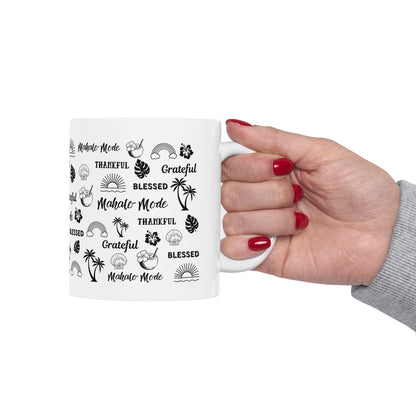 A white ceramic mug with black tropical-themed text and illustrations, held by a hand with red nail polish against a plain white background.