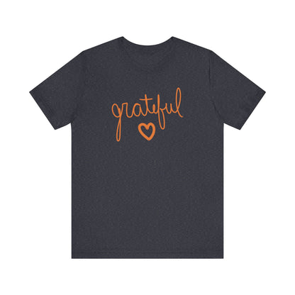A navy heather t-shirt with the word 'grateful' written in orange cursive script and a matching orange heart outline below it, displayed on a solid white background.
