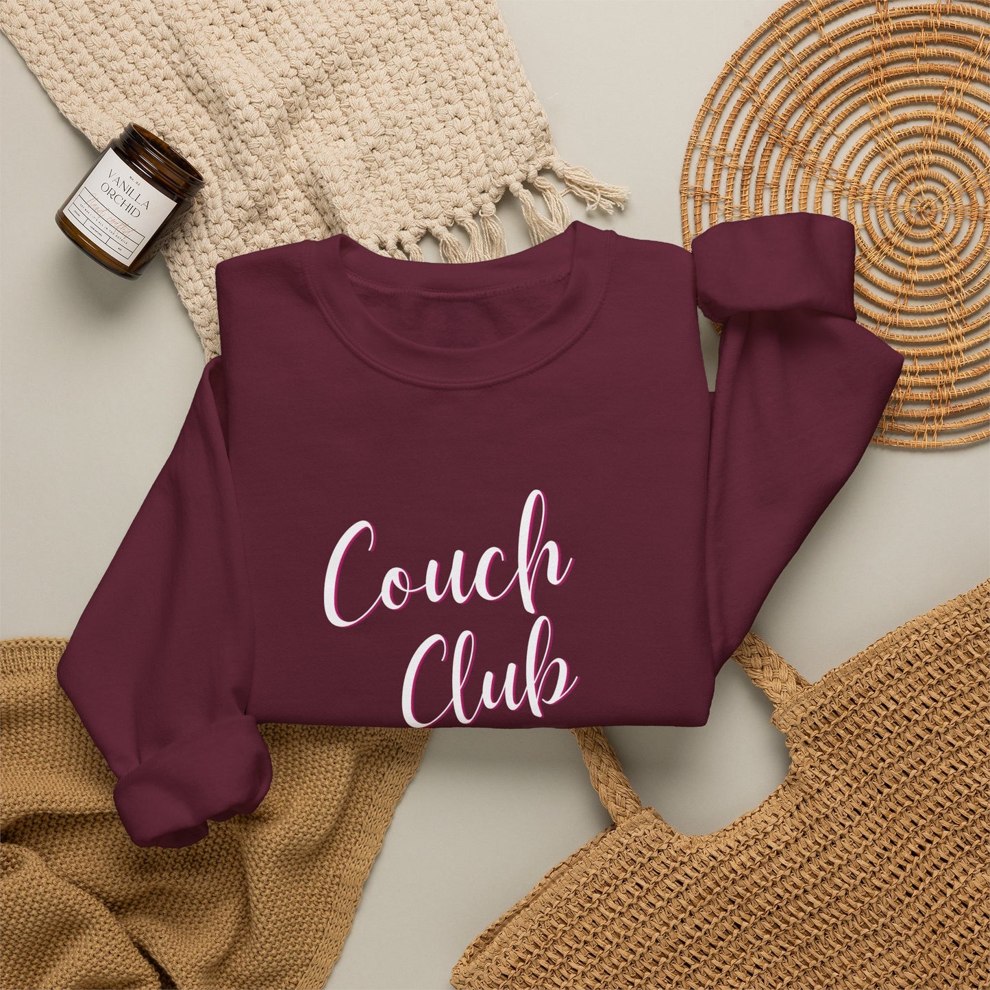 Folded maroon sweatshirt with a graphic design text 'Couch Club' on a textured surface