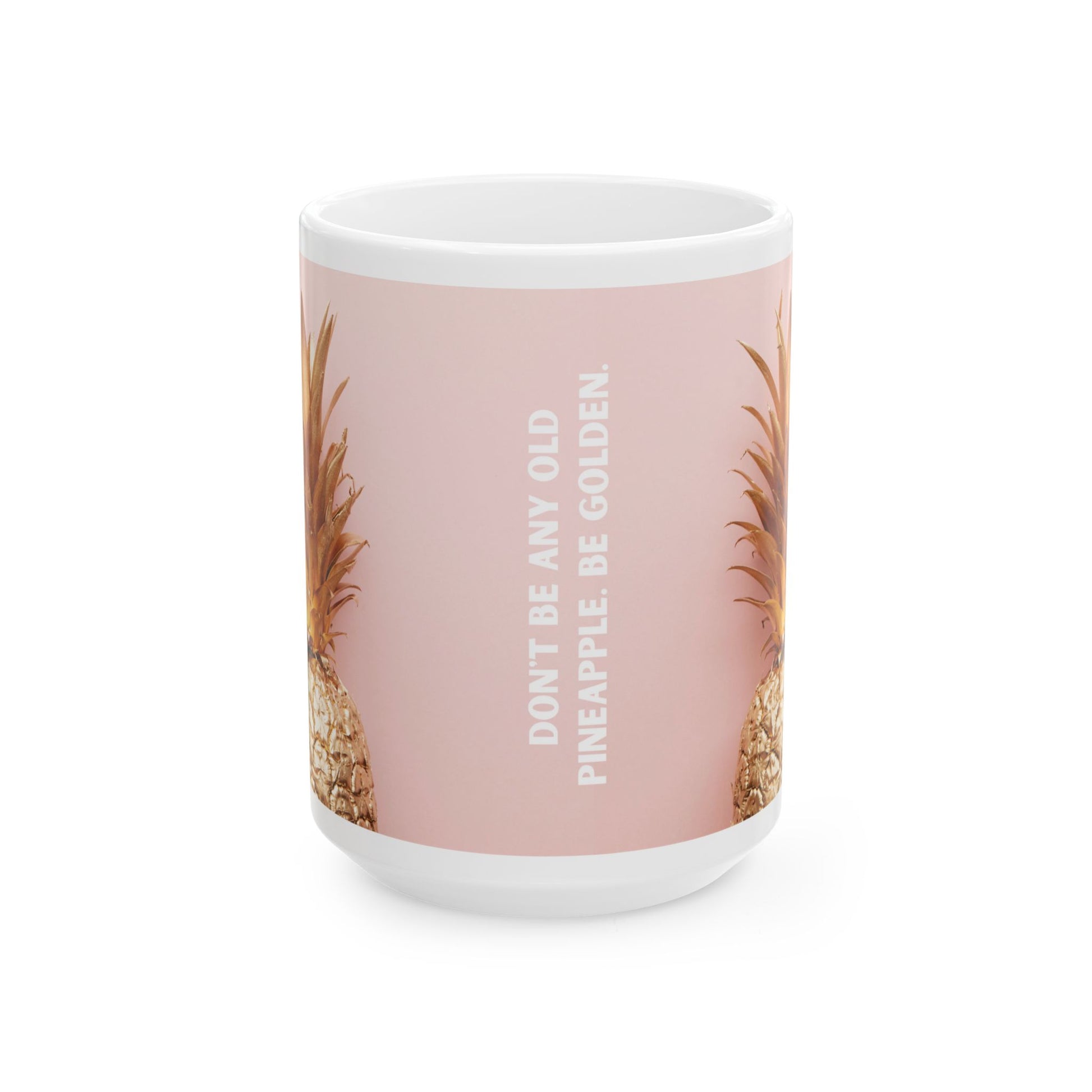 A white ceramic mug with a dusty pink wraparound design featuring partial pineapples on both sides and the vertical text 'DON'T BE ANY OLD PINEAPPLE, BE GOLDEN.' on the front.