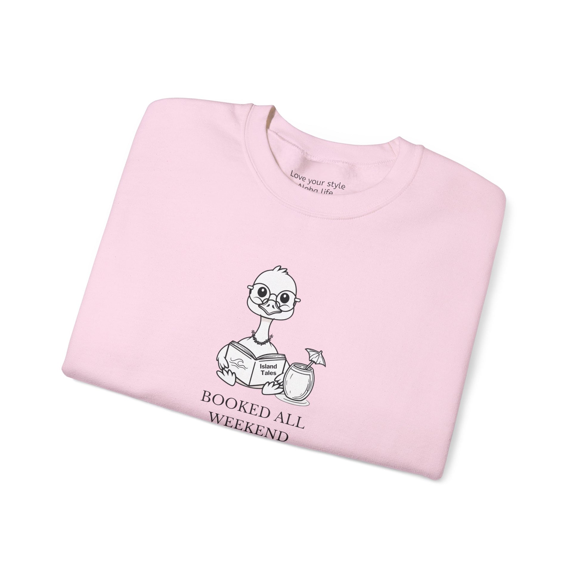 A folded light pink crewneck t-shirt featuring a cartoon nene goose character reading a book with the text 'BOOKED ALL WEEKEND' underneath, displayed on a clean white background.