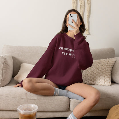 Person wearing a maroon sweatshirt with a graphic print 'champagne crew', sitting on a couch in a living room.