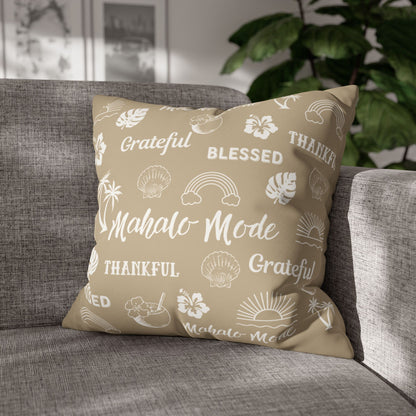 A square throw pillow with a beige background and white tropical-themed text and illustrations, resting on a gray fabric sofa in a living room setting with a green plant in the background.