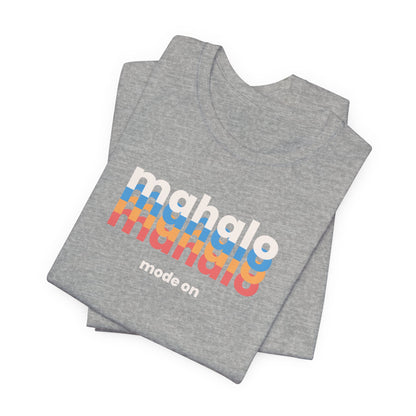A folded heather gray t-shirt with a retro-style graphic reading 'mahalo manalo' in white, blue, orange, and red stripes, with 'mode on' printed below in white, shown on a plain white background.