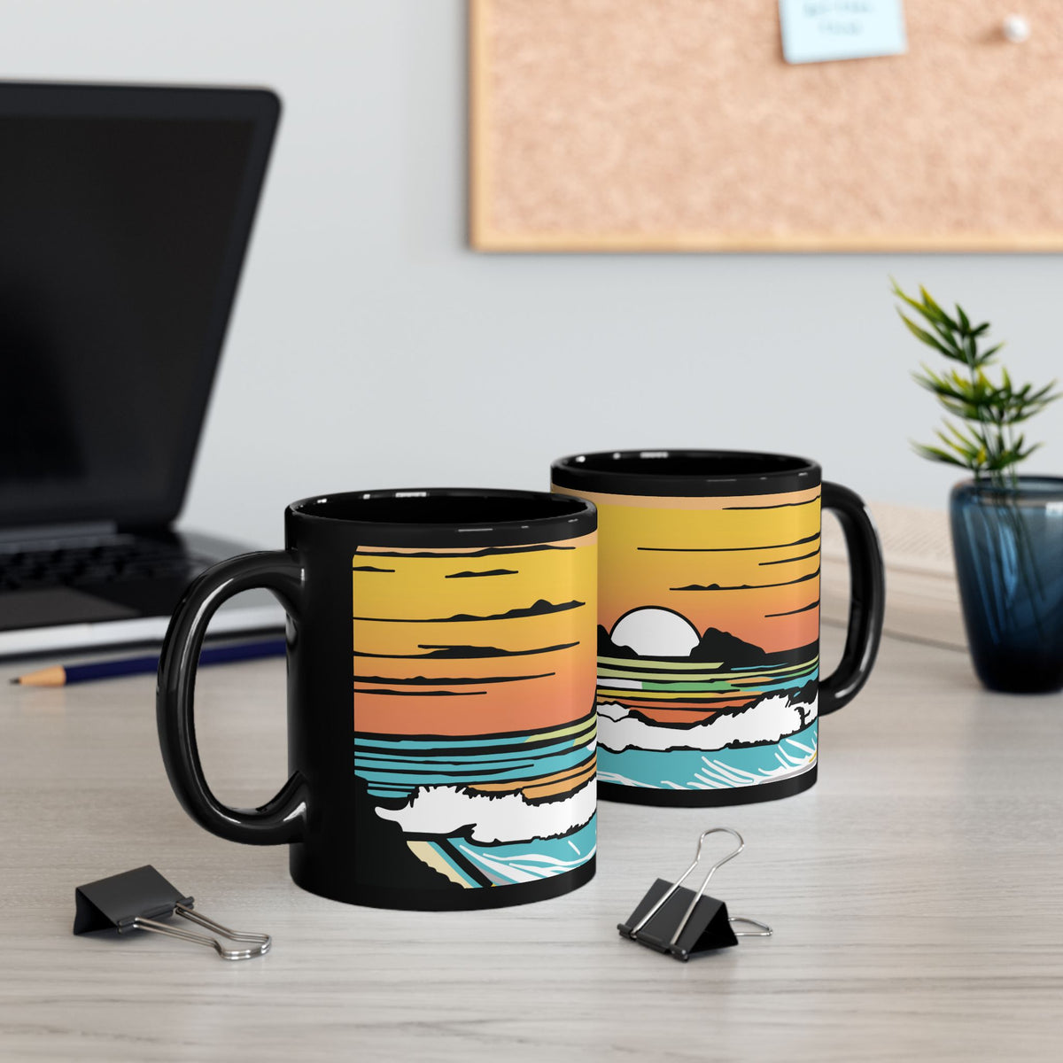 Two black ceramic mugs with a colorful retro Hawaii sunset and ocean wave illustration, displayed on a light wood desk with office props in the background.