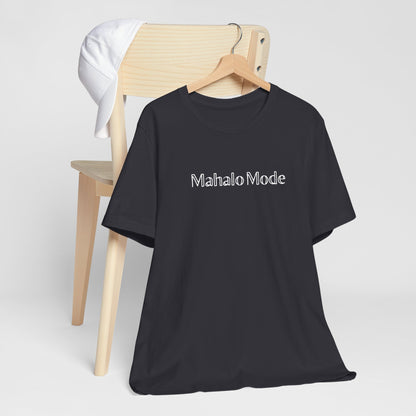 A Mahalo Mode graphic tee in dark grey heather with white outlined lettering, Global Village Kailua original design, hanging from a wooden chair.