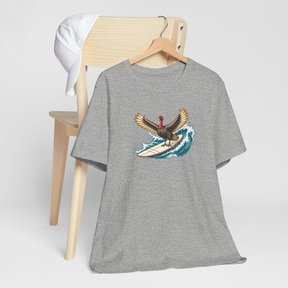 Athletic gray surfing turkey Thanksgiving T-shirt featuring a teal wave and vintage-inspired island artwork hanging off a light wooden chair.