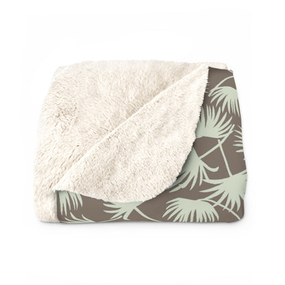 A folded plush throw blanket with a cream sherpa sherpa-style sherpa side and a taupe side featuring a sage green palm leaf pattern.
