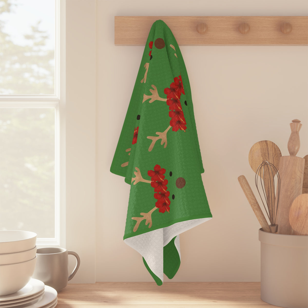 Green Reindeer and Rudolph holiday kitchen towel with red nose design hanging off a wood peg on a kitchen wall