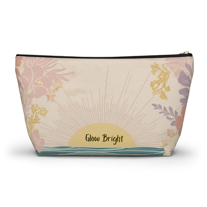 A rectangular zippered pouch with a tropical sunset print, featuring pink and purple flowers, a yellow sunburst, and the text 'Glow Bright' on a cream background.