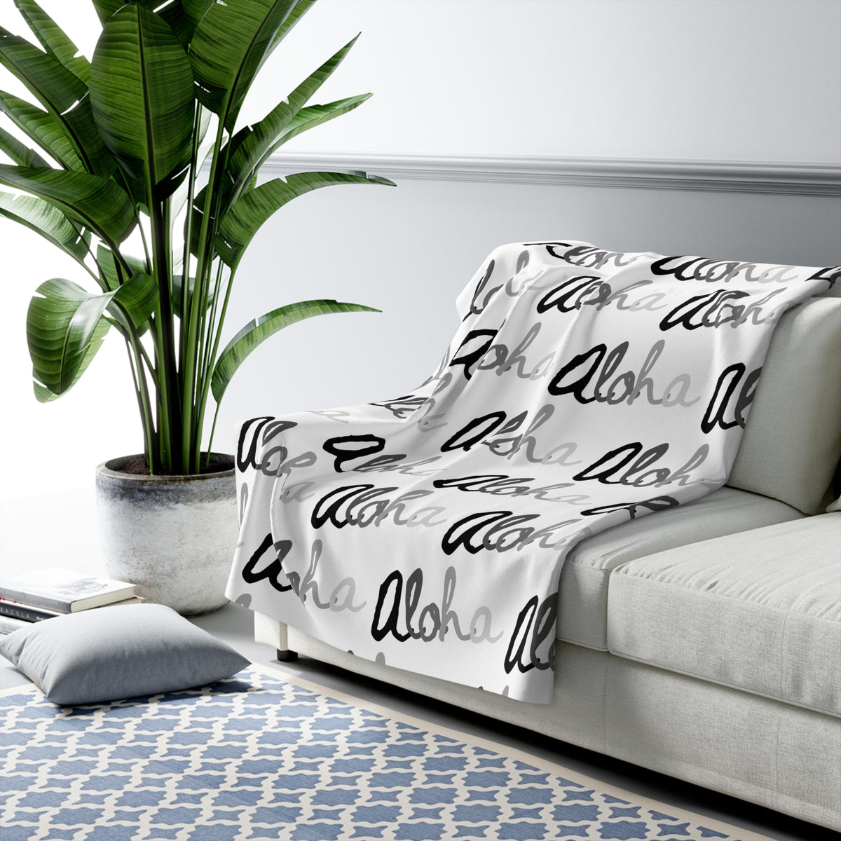 Aloha grayscale sherpa fleece blanket with a repeating black, white and gray island-inspired design draped over a grey couch.