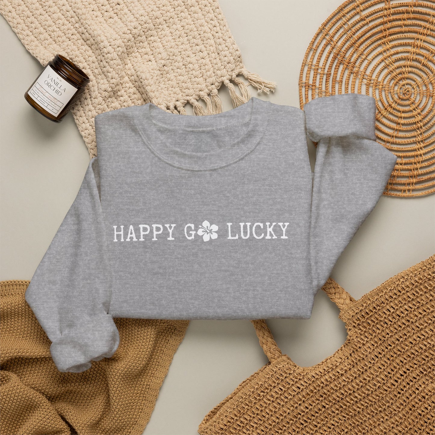 Gray sweatshirt with 'HAPPY GO LUCKY text on a textured surface with a bottle and woven mat.