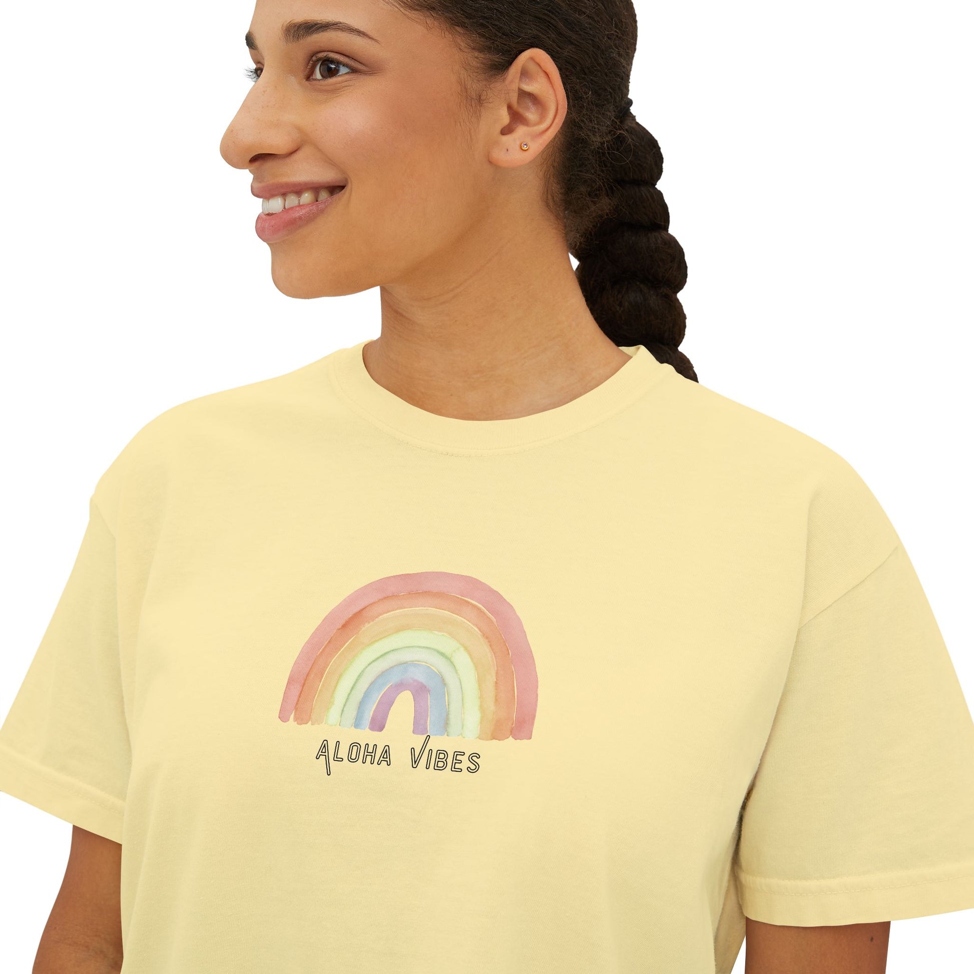 A woman wearing a pale yellow t-shirt with a watercolor rainbow graphic and the text 'ALOHA VIBES' printed on the chest, shown against a plain white background.