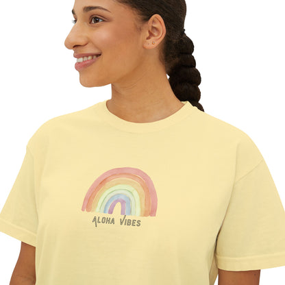 A woman wearing a pale yellow t-shirt with a watercolor rainbow graphic and the text 'ALOHA VIBES' printed on the chest, shown against a plain white background.
