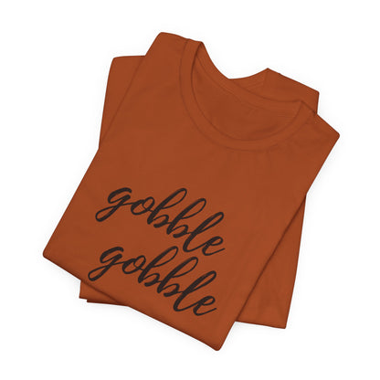 A folded rust t-shirt with the phrase 'gobble gobble' printed in black cursive script across the front, displayed on a clean white background.