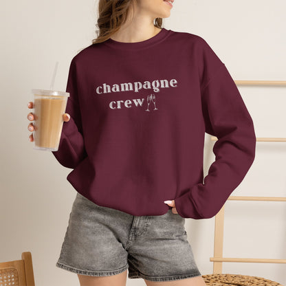 Woman wearing a maroon graphic sweatshirt with text 'champagne crew' in white letters holding an iced coffee