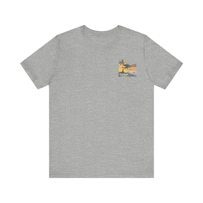 A heather grey short-sleeve t-shirt with a vintage-style graphic on the front left chest depicting two palm trees against a yellow and orange sunset, with the text 'ná makulua' and 'Kailua, Hawaii!' printed below.