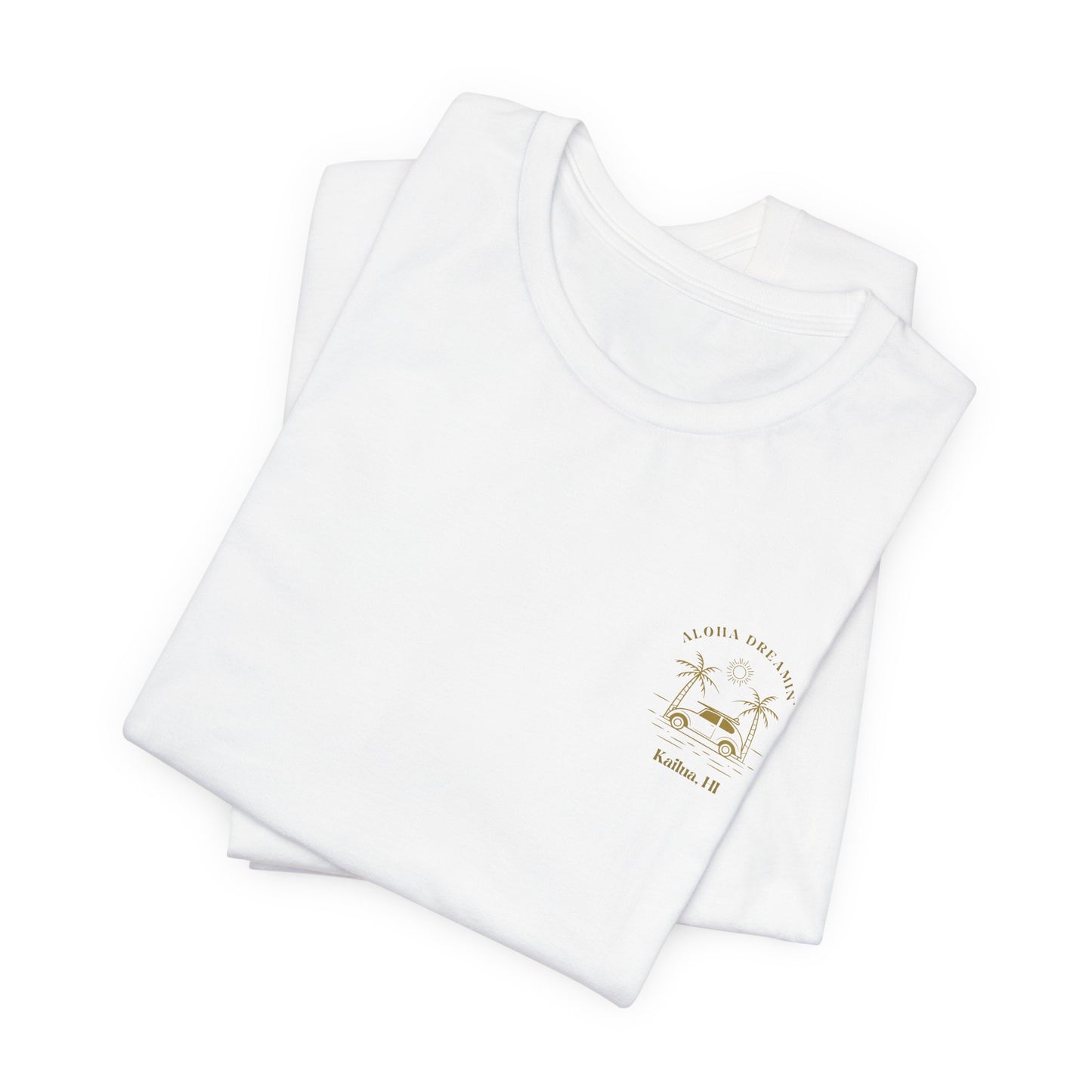 A folded white short-sleeve t-shirt shown from the front, featuring a gold-colored retro graphic of a classic car between two palm trees with the text 'ALOHA DREAMIN'' and 'Kailua, HI' on the left chest.