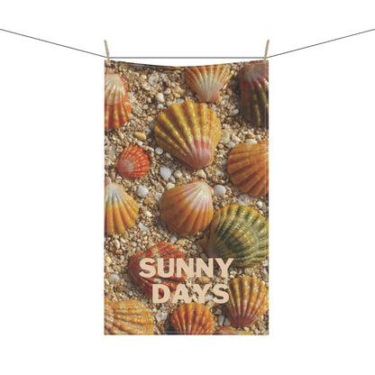 A rectangular teatowel printed with seashells on sandy ground and the words “SUNNY DAYS,” hanging from a string with two wooden clips against a white background.