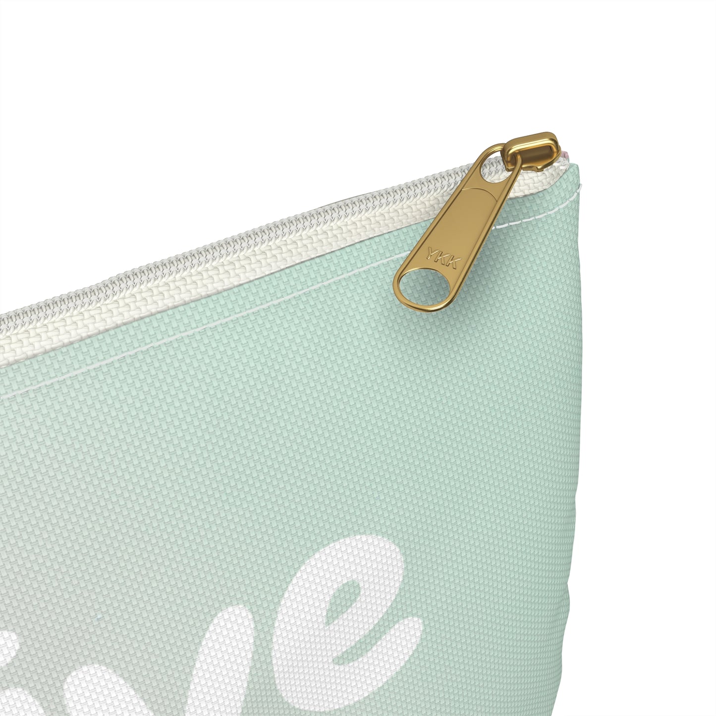 A close-up of a mint green canvas pouch with a white zipper and a gold-tone metal pull tab, featuring a partial white script graphic on the front.