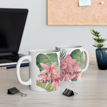Two white ceramic mugs with pink tropical flowers and green leaves printed on them, displayed on a light wood desk with office props in the background.