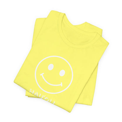 A folded bright yellow t-shirt with a white smiley face graphic and the word 'HAUʻOLI HAPPY' printed in white near the bottom, displayed on a clean white background.