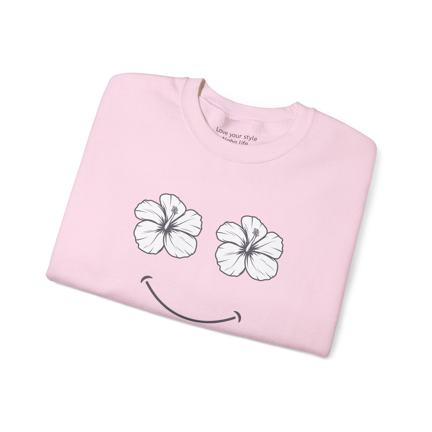 A folded light pink t-shirt with a graphic of two white hibiscus flowers forming eyes and a black smiley mouth, shown on a plain white background.