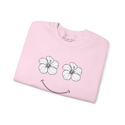 A folded light pink t-shirt with a graphic of two white hibiscus flowers forming eyes and a black smiley mouth, shown on a plain white background.