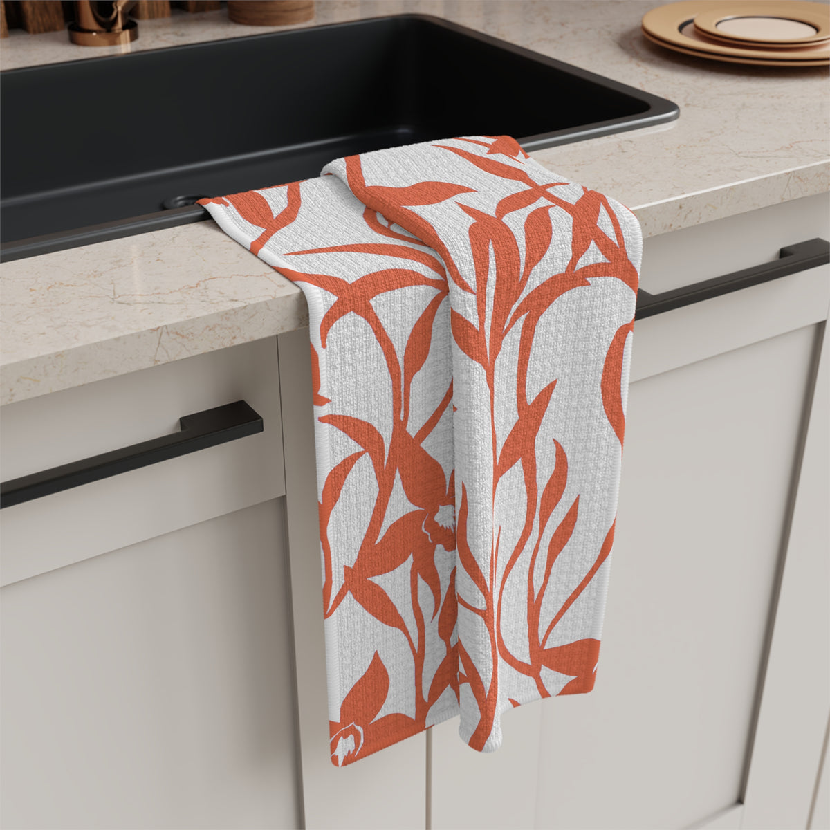 A rectangular white kitchen towel or tea towel featuring a bold coral orange floral pattern of orchids and leaves, shown flat against a solid white background hanging off of a sink.