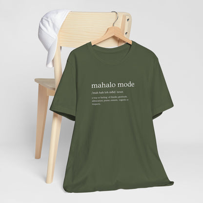 A military green t-shirt with a white printed dictionary-style definition of 'mahalo mode' on the chest, hanging from a wooden chair