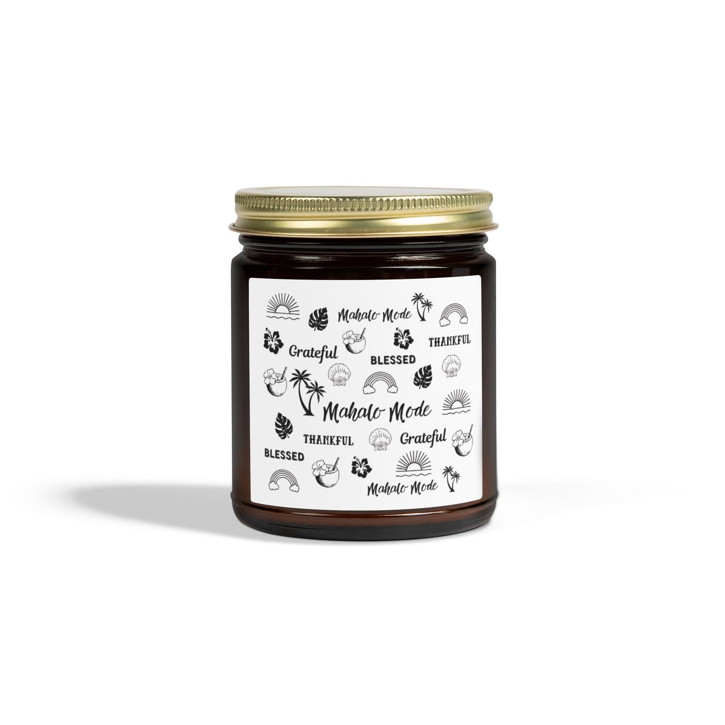 A dark amber glass jar candle with a gold metal screw-on lid and a white paper label featuring black hand-drawn style illustrations and the words 'Mahalo • Mode', 'Grateful', 'BLESSED', and 'THANKFUL'.
